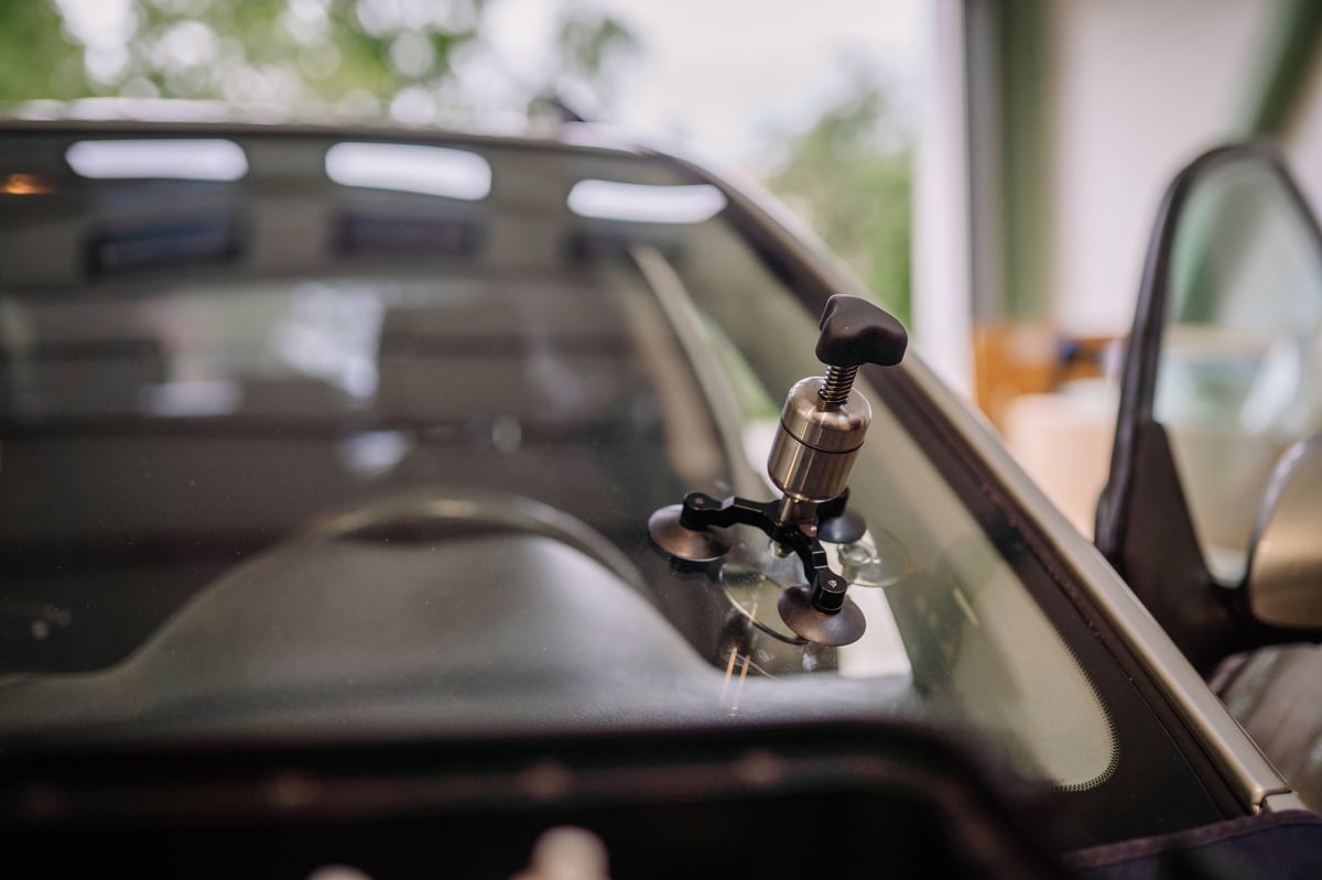 Windshield repair bridge tool with suction cups and a metal injector handle positioned on a car's glass inside a garage
